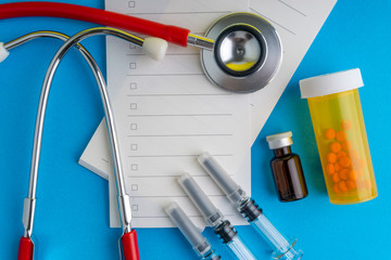 Medical syringe, stethoscope, vials, ampule and notebook on blue background with selective focus...