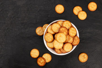 An overhead photo of salt crackers in a bowl, shot from above on a black background with a place for text