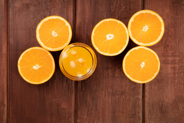 A photo of a glass of fresh orange juice with orange halves, shot from the top on a dark rustic wooden background with a place for text