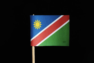 A national flag of Namibia on toothpick on black background. A consists of a white-edged red diagonal band radiating from the lower hoist side corner. The upper is blue with yellow sun and lower green