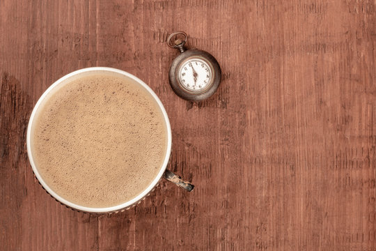 Coffee Time, vintage style. An overhead photo of coffee in a retro cup, shot from the top on a dark rustic wooden background with an old watch and copy space. Toned image