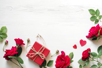 Red roses flowers, gift red box with a bow and hearts on a white wooden background, copy space, top view. Festive romantic background for Valentine's Day