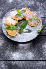 Cottage cheese pancakes with fresh mint sprinkled with powdered sugar. Syrniki on dark wooden boards. Healthy food for breakfast. Dish of milk products. Copy space