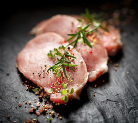 Slices of raw pork loin with the addition of aromatic herbs and spices on a black stone background