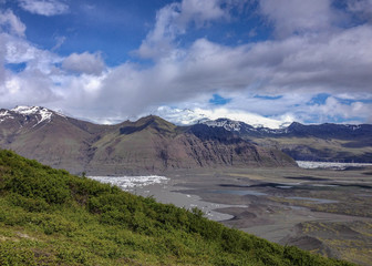 Mountain range Hafrafell covered with snow, glacier tongue Skaftafellsjokull and green forest with blue sky in summer, Vatnajokull National Park, South Iceland
