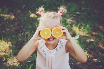 Little girl holding oranges in front of her eyes.