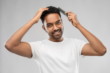 grooming, hairstyling and people concept - smiling young indian man brushing hair with comb