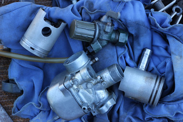 Parts from a disassembled motorcycle: a carburetor, pistons and a fuel tap with a pipe.