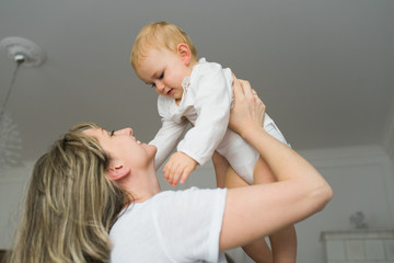 Happy smiling mother holding her baby up in her arms. Mommy and baby playing together in the...