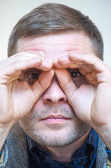 Man looking through fingers like through imaginary binoculars