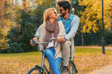 Obraz premium Happy young couple having fun riding a bicycle on sunny day in the park.