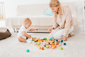 adorable toddler playing with colorful cubes and mother in nursery room