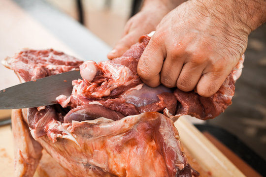 Raw lamb cutting, cook hands with knife