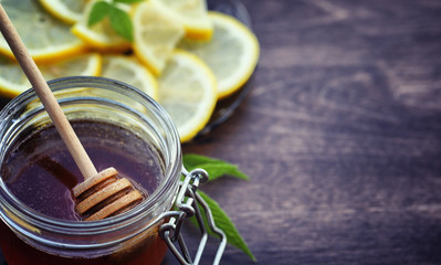Tea with lemon and mint in nature. A cup of hot mint tea with lemon and honey in a jar. Lemon slices and a spoon with honey to hot tea.