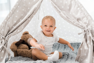 smiling adorable toddler sitting in baby wigwam with fluffy teddy bear toy © LIGHTFIELD STUDIOS