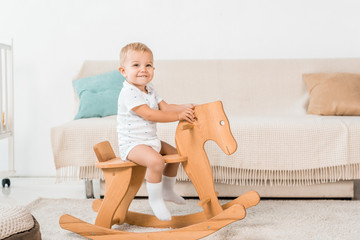 adorable smiling toddler sitting on toy wooden horse