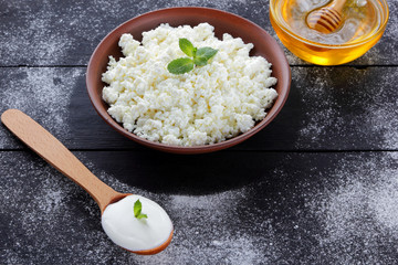 Cottage cheese in clay bowl and honey on wooden boards. Sour cream in wooden spoon. Dairy products and honey on dark background. Fresh mint and soft cheese for breakfast