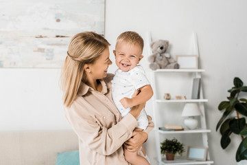 Obraz na płótnie Canvas cheerful mom holding smiling son in nursery room