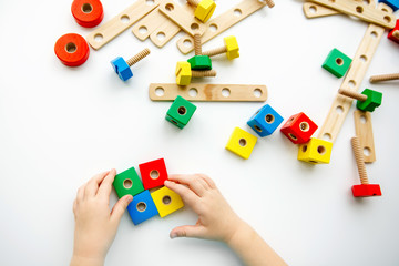 Obraz premium Close up of child hands playing with colorful wooden bricks at the table. Toddler having fun and building out of bright constructor bricks. Early learning. Top view. Flat lay.