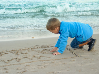 Little boy draws on sand