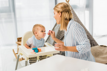 Fototapeta premium mom feeding son in highchair with baby food