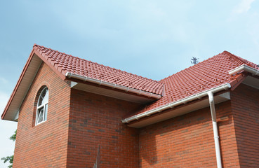 Rain gutter pipe system. Close up on attic brick house with clay roof tiles and plastic roof gutter...