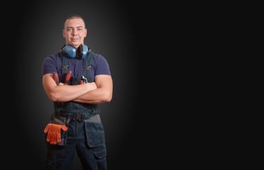 Strong male mechanic in blue overal standing on a black background