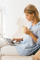 Fototapeta premium side view on adult woman holding cup of tea and using laptop