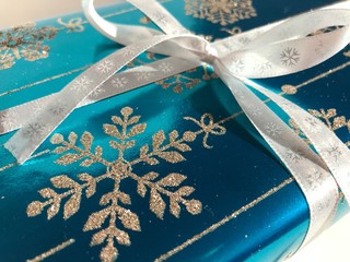 Christmas gift wrapped in blue metallic paper with silver glitter snowflakes and decorated with a ribbon tied in a bow.