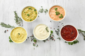 Different tasty sauces in bowls with spices on white wooden table