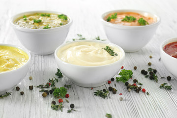 Different tasty sauces in bowls with spices on white wooden table