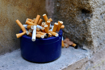 Blue ashtray full of cigarette butts on stone window