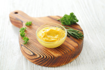 Tasty yellow sauce in bowl with herbs on white wooden table