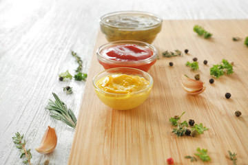 Different tasty sauces in bowls with spices on wooden board