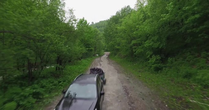 One black SUV with trailer driving on winding dirty road in forest mountains - Aerial Drone View