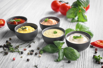 Different tasty sauces in bowls with spices on light wooden table - obrazy, fototapety, plakaty