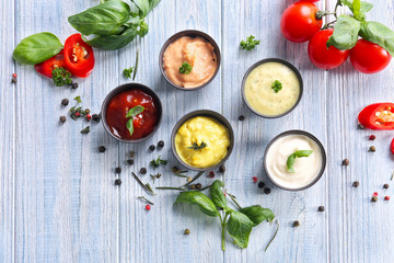 Different tasty sauces in bowls with spices on light wooden table