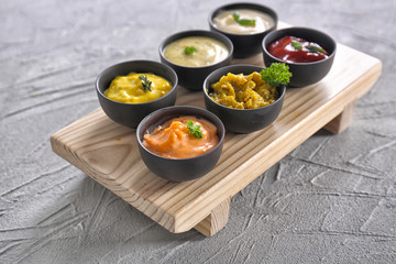 Different tasty sauces in bowls on wooden board