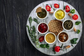 Different tasty sauces in bowls with waffles on wooden table