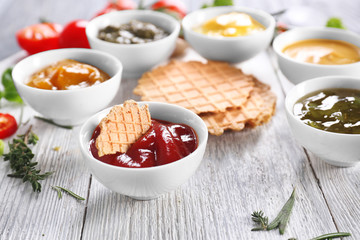 Different tasty sauces in bowls with waffles on wooden board