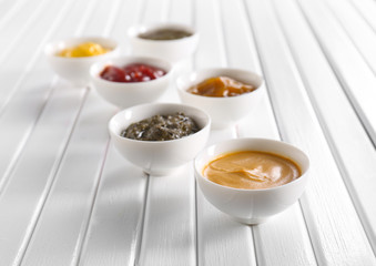 Different tasty sauces in bowls on white wooden table