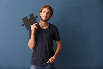 Thoughtful young man with piece of jigsaw puzzle on color background