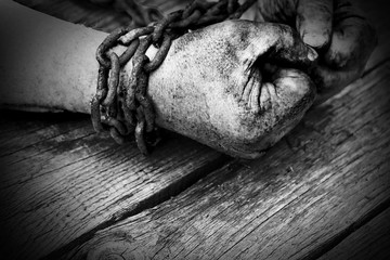 Powerful dirty male hands clenched into fists chained with rusty chain. Black and white photo.