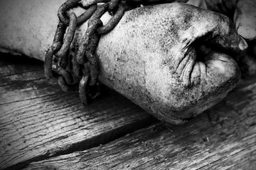Powerful dirty male hands clenched into fists chained with rusty chain. Black and white photo.