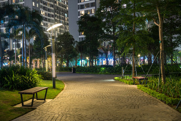 Garden walkway with lamps at night. Tree and building on background