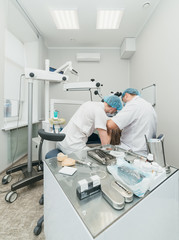 Doctor used microscope. Dentist is treating patient in modern dental office. Operation is carried out using cofferdam. Client is inserted and restored teeth, make denture. Orthodontist and assistant
