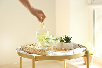 Woman putting frozen cucumber slice into glass on table