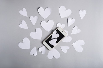 Paper hearts and mobile phone on grey background