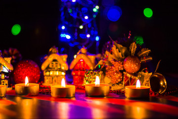 Merry Cristmas. Toy houses and candlelight. Christmas decorations on blurred background. Festive evening. Spruce branches and Christmas toys with bokeh. Copy space