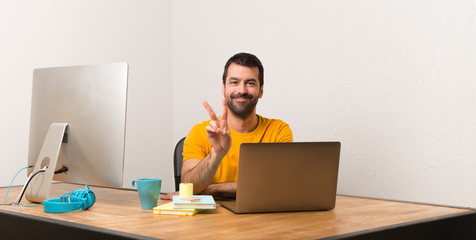 Man working with laptot in a office smiling and showing victory sign